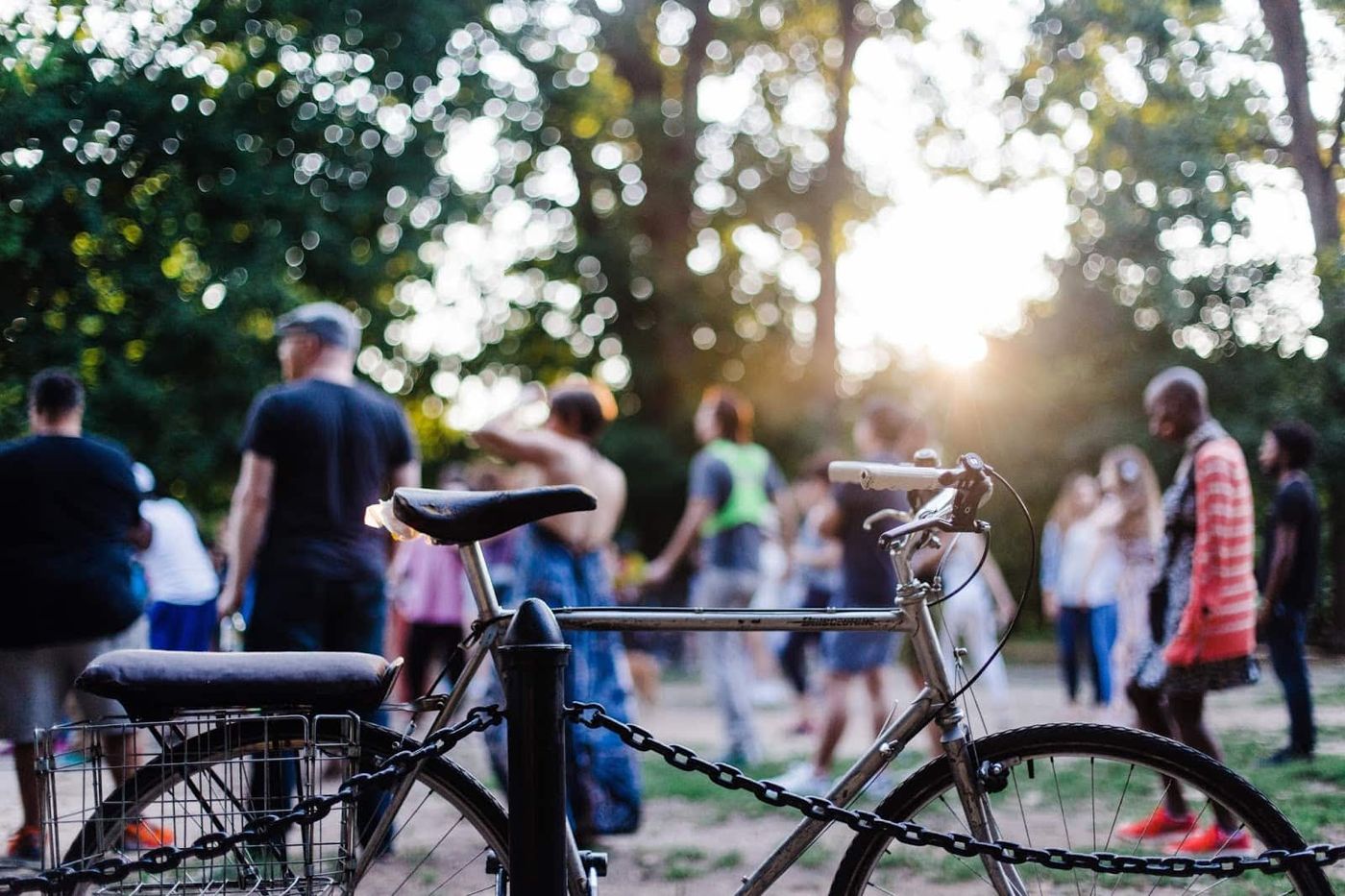 Vélo attaché à un poteau dans un parc au coucher du soleil, avec des personnes rassemblées en arrière-plan
