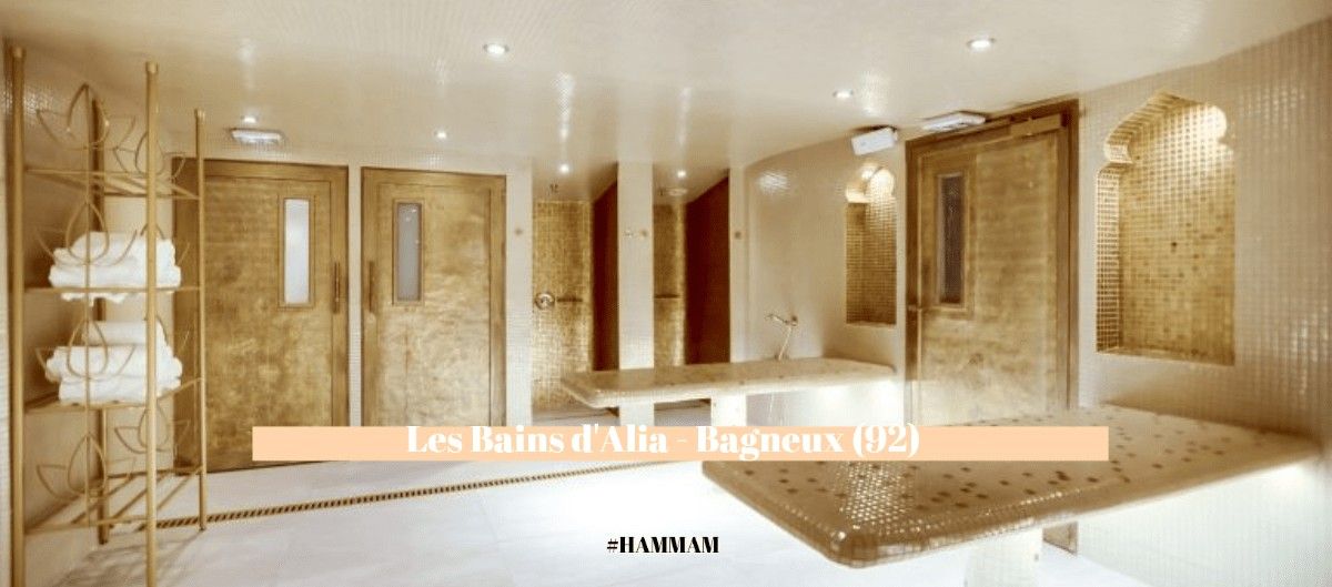 Intérieur d'un hammam aux mosaïques et portes dorées avec tables en pierre et serviettes blanches