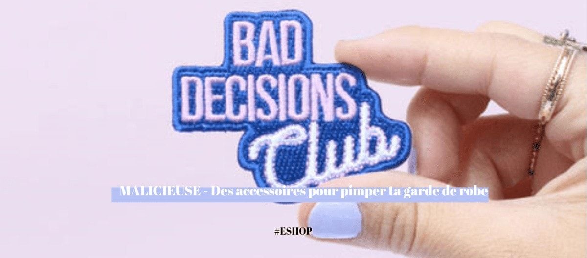 Une main tenant un écusson brodé « Bad Decisions Club » sur fond mauve.