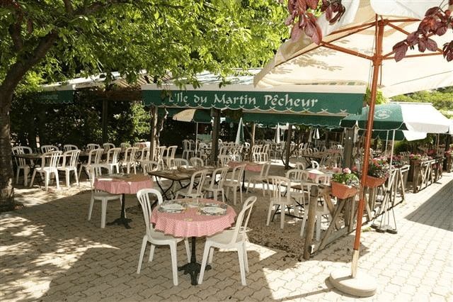 Terrasse ombragée de la guinguette L'Île du Martin-Pêcheur, avec tables à nappes vichy rouges et parasols.