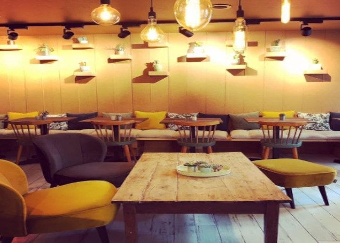 Salle intérieure chaleureuse d'un restaurant avec fauteuils jaunes et gris, tables en bois et ampoules suspendues