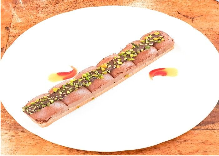Dessert allongé au chocolat parsemé de pistaches concassées sur une assiette blanche