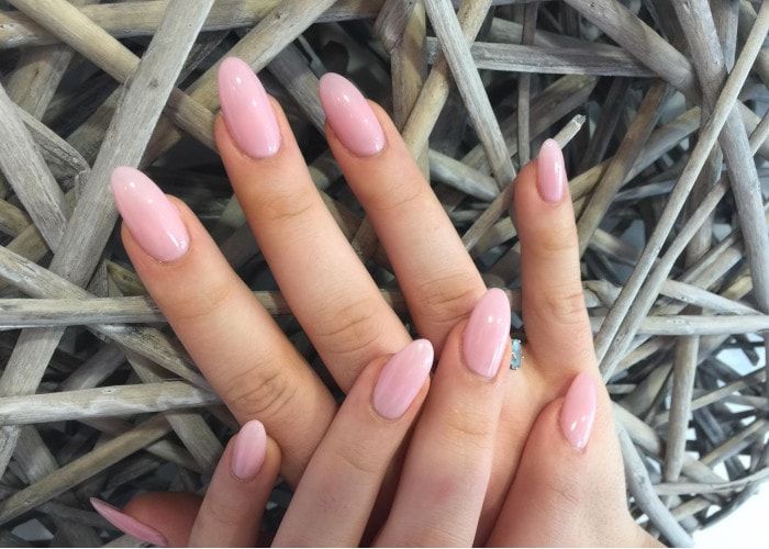 Deux mains aux ongles ovales manucurés vernis rose posées sur des branches de bois flotté.
